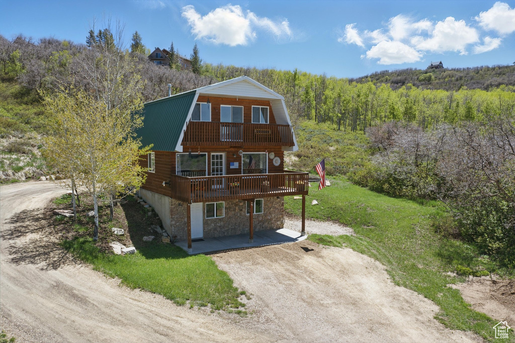 View of front of home featuring a gambrel roof, stone siding, a wooded view, dirt driveway, and metal roof