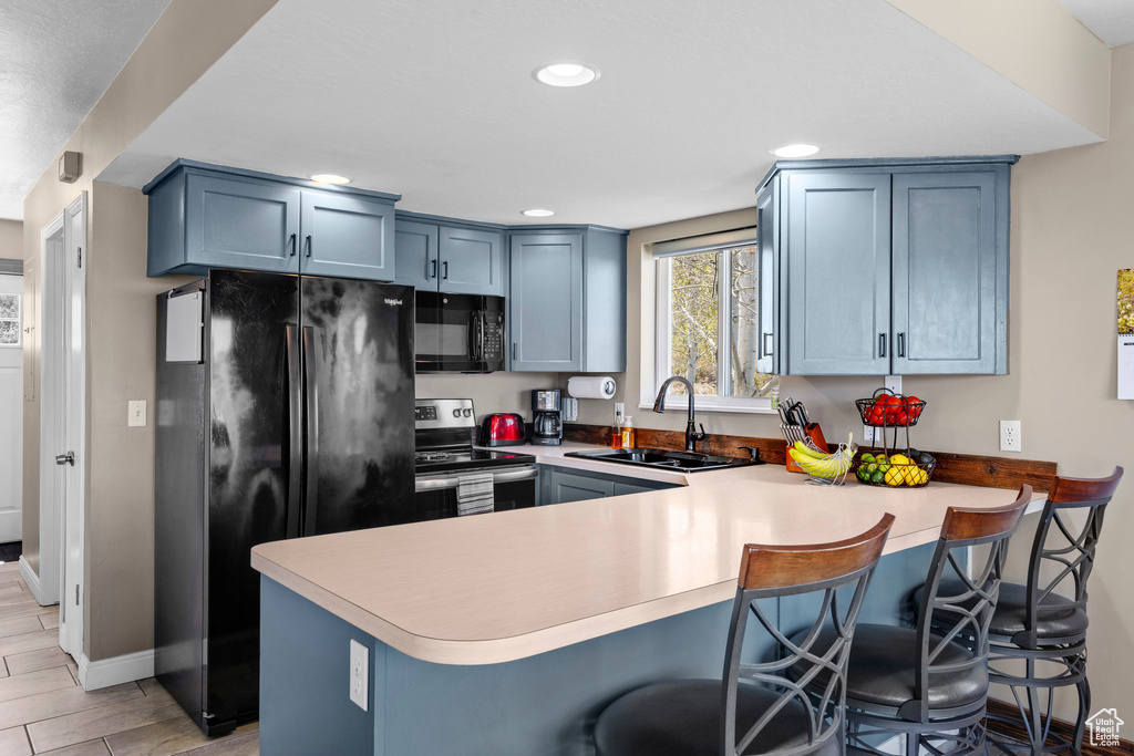 Kitchen with black appliances, a sink, a peninsula, blue cabinets, and recessed lighting