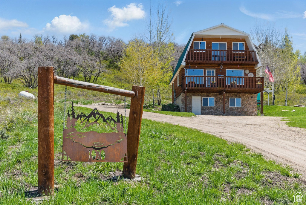 View of front of home featuring a balcony, a gambrel roof, stone siding, and driveway