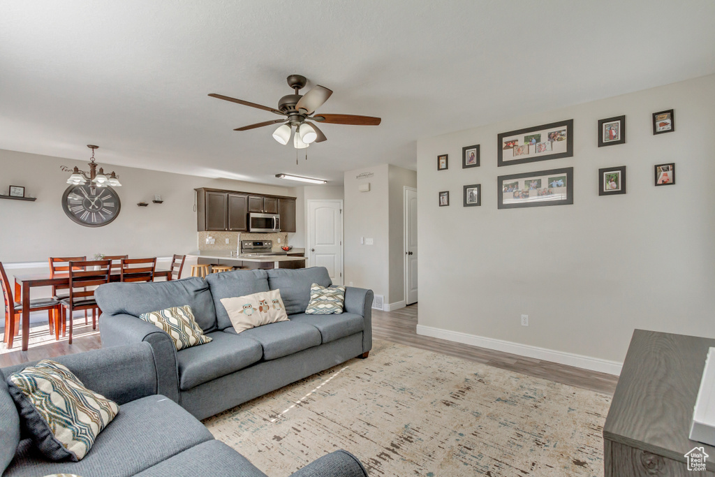 Living area featuring light wood finished floors, a chandelier, a ceiling fan, and baseboards