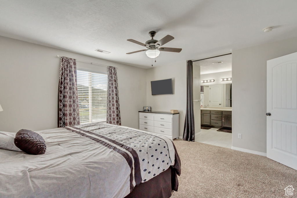 Bedroom with light carpet, ensuite bath, and a ceiling fan