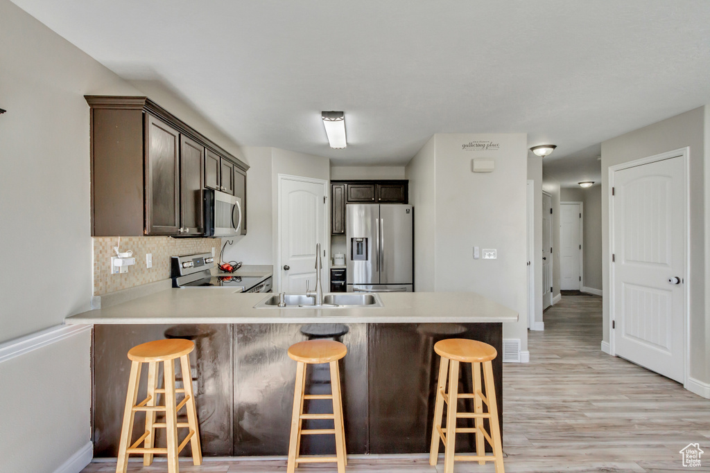 Kitchen featuring stainless steel appliances, a sink, a peninsula, dark brown cabinets, and light countertops