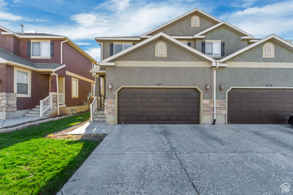View of front facade featuring driveway, stucco siding, an attached garage, and a front yard