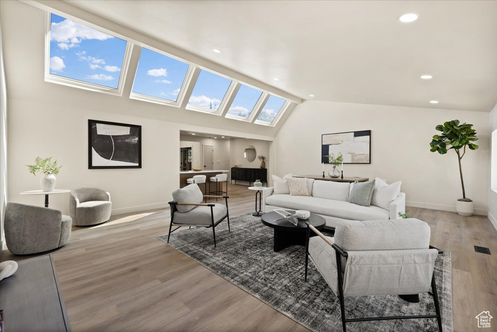 Living room featuring a skylight, baseboards, light wood finished floors, lofted ceiling, and recessed lighting
