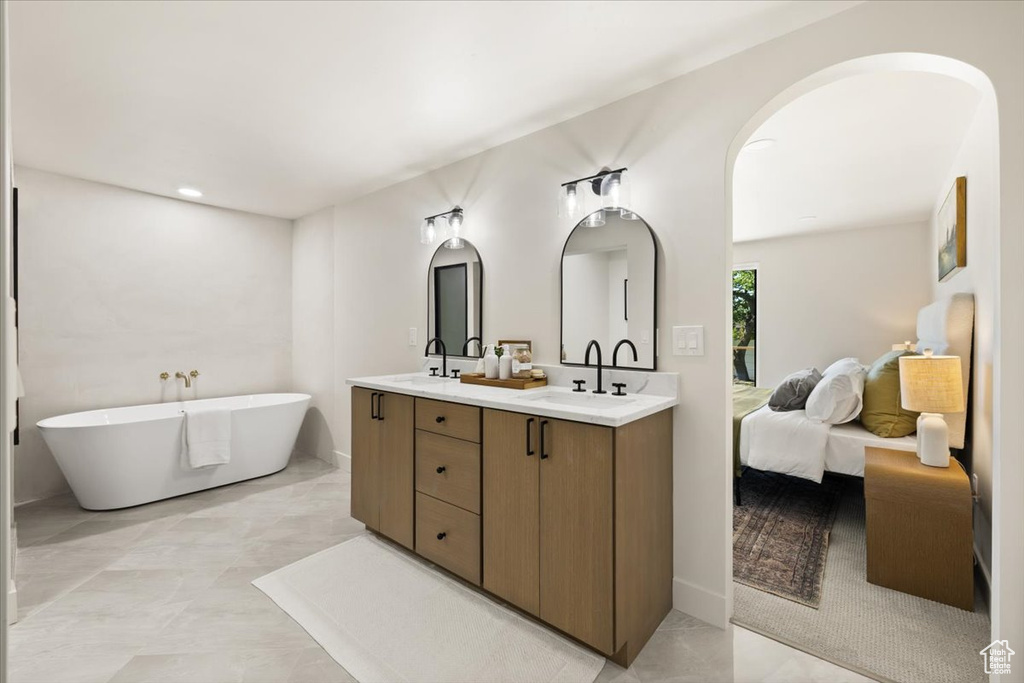 Ensuite bathroom with double vanity, a soaking tub, and marble look tile flooring