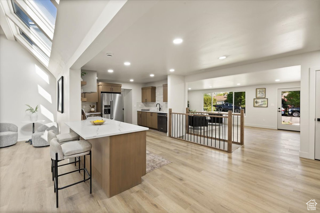 Kitchen with high quality fridge, black dishwasher, open floor plan, a kitchen breakfast bar, and light wood-style floors