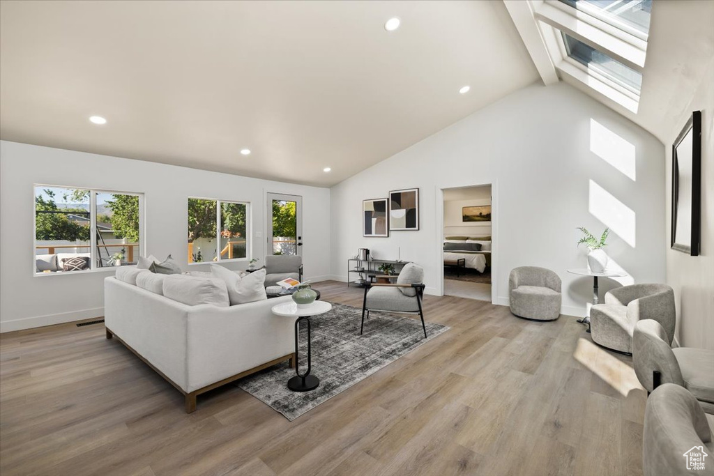 Living area with healthy amount of natural light, recessed lighting, light wood-style floors, high vaulted ceiling, and baseboards