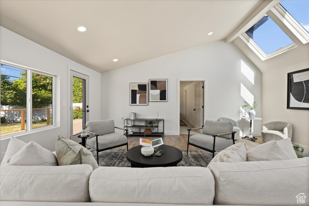 Living room with lofted ceiling, a skylight, wood finished floors, recessed lighting, and baseboards