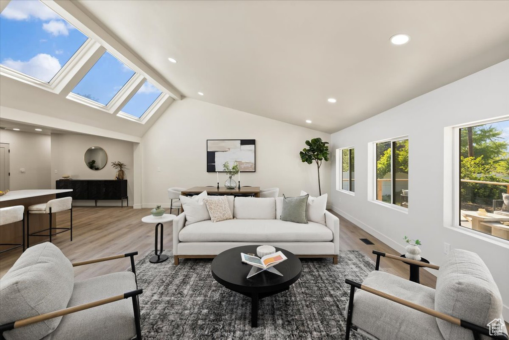 Living area with a skylight, lofted ceiling, wood finished floors, recessed lighting, and baseboards