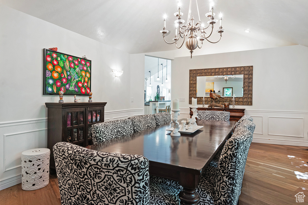 Dining room with wood finished floors, a decorative wall, a chandelier, a wainscoted wall, and vaulted ceiling