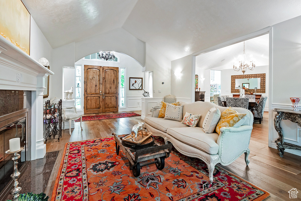 Living room featuring a chandelier, arched walkways, wood finished floors, a tiled fireplace, and high vaulted ceiling