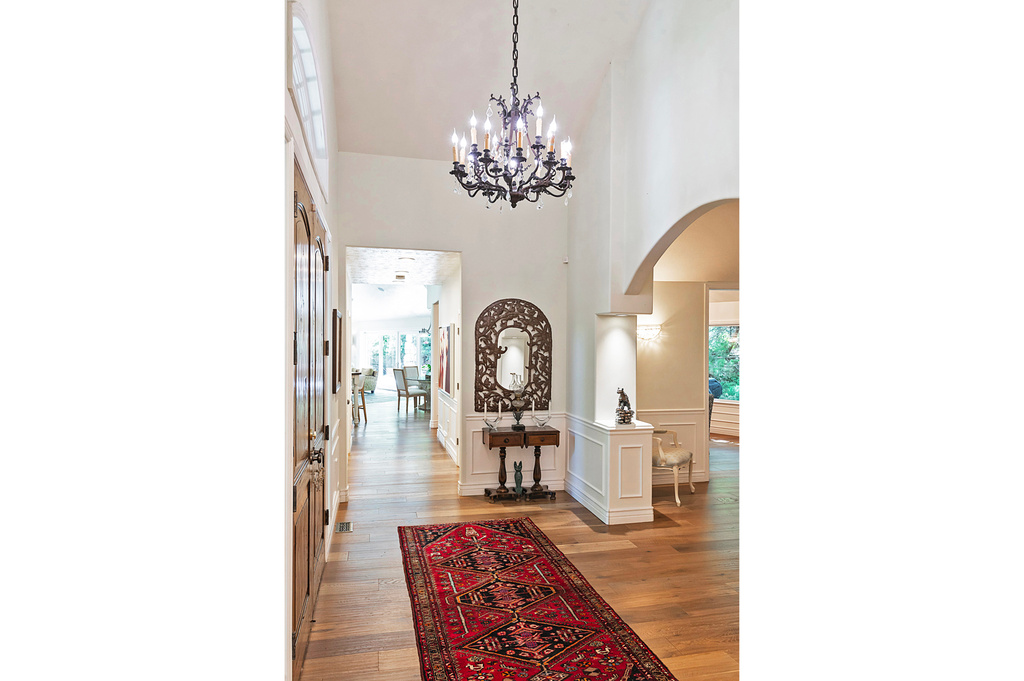 Hall with arched walkways, a high ceiling, light wood-style flooring, a chandelier, and wainscoting