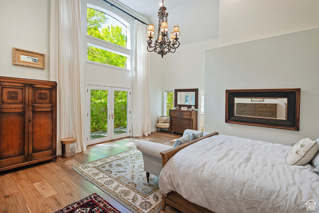 Bedroom with a high ceiling, access to exterior, a chandelier, and wood finished floors