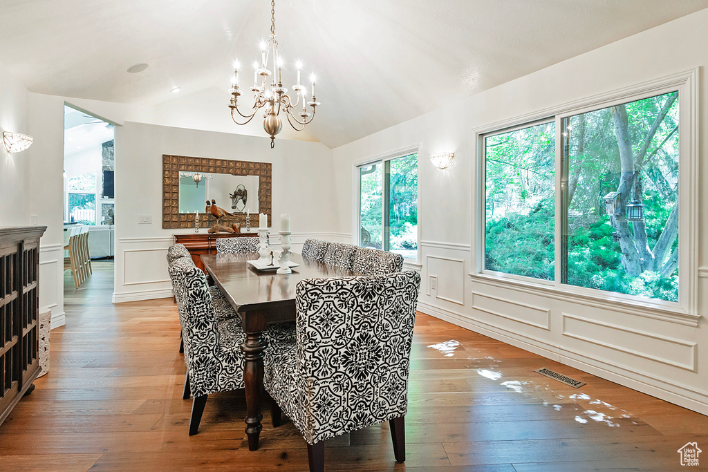 Dining area featuring a decorative wall, a chandelier, light wood-type flooring, wainscoting, and vaulted ceiling