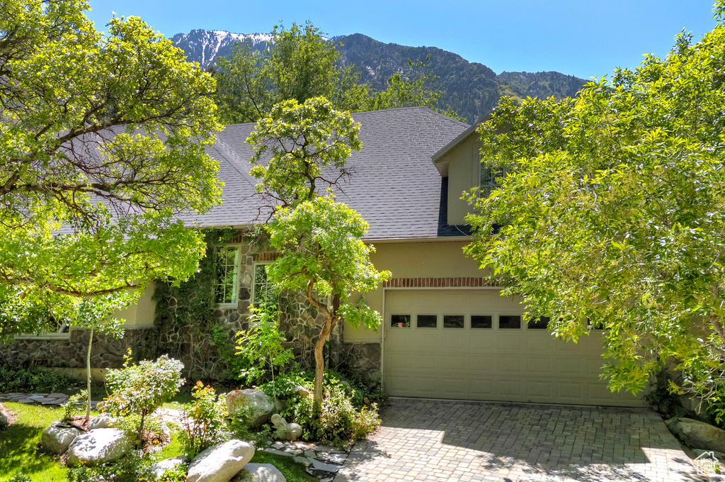 Obstructed view of property featuring stone siding, a shingled roof, a mountain view, and decorative driveway