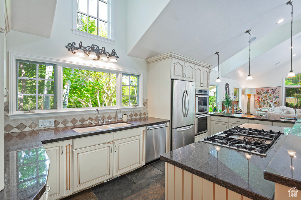 Kitchen featuring stainless steel appliances, a sink, high vaulted ceiling, stone tile flooring, and healthy amount of natural light