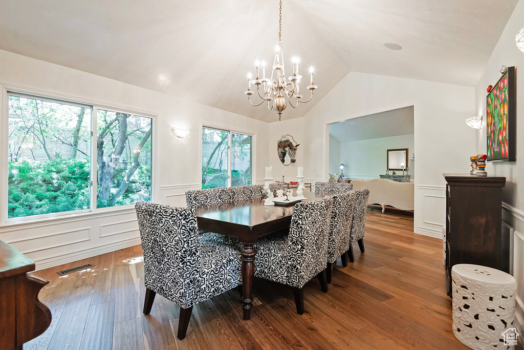 Dining room with a chandelier, wainscoting, a decorative wall, wood finished floors, and lofted ceiling