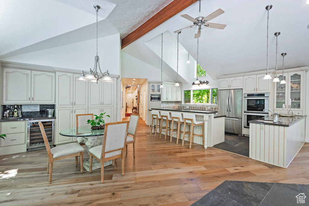 Dining room featuring beverage cooler, high vaulted ceiling, beamed ceiling, ceiling fan, and light wood finished floors