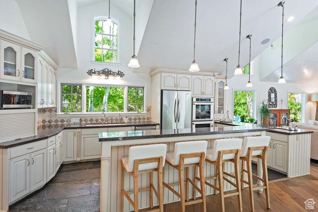 Kitchen with appliances with stainless steel finishes, high vaulted ceiling, a sink, a center island, and glass insert cabinets