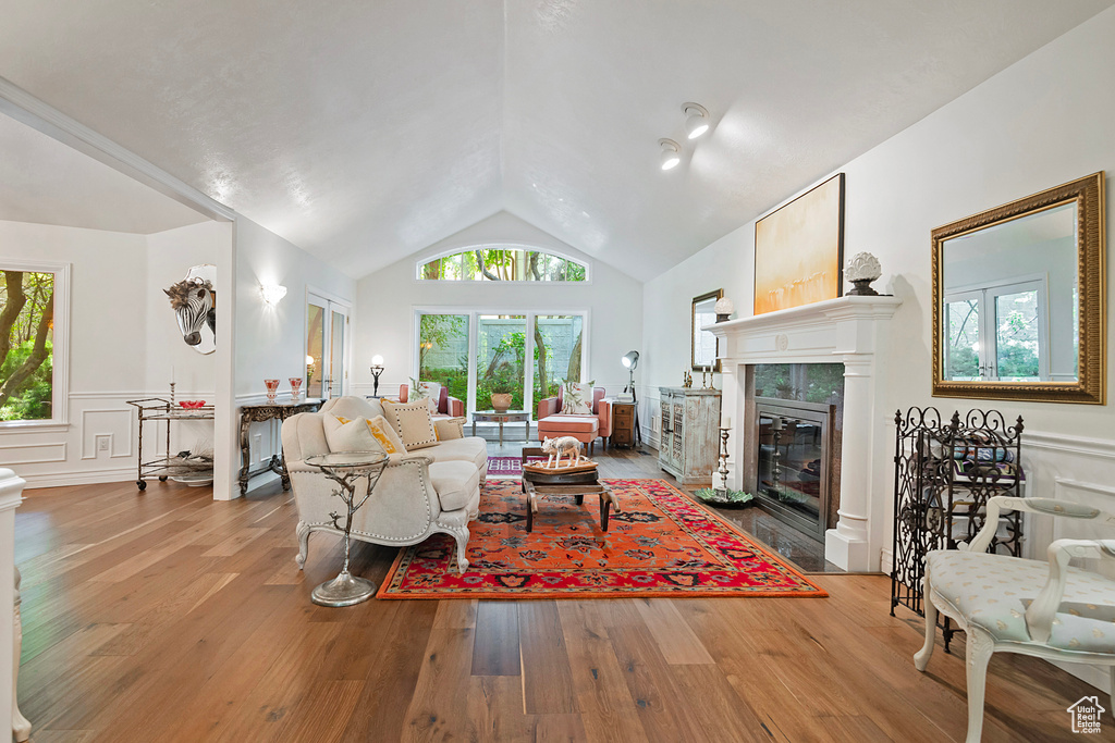 Living area with plenty of natural light, lofted ceiling, wood finished floors, and a tiled fireplace