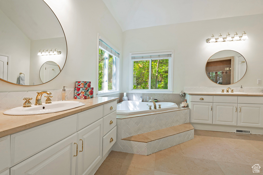 Full bathroom with two vanities, lofted ceiling, a garden tub, and tile patterned floors
