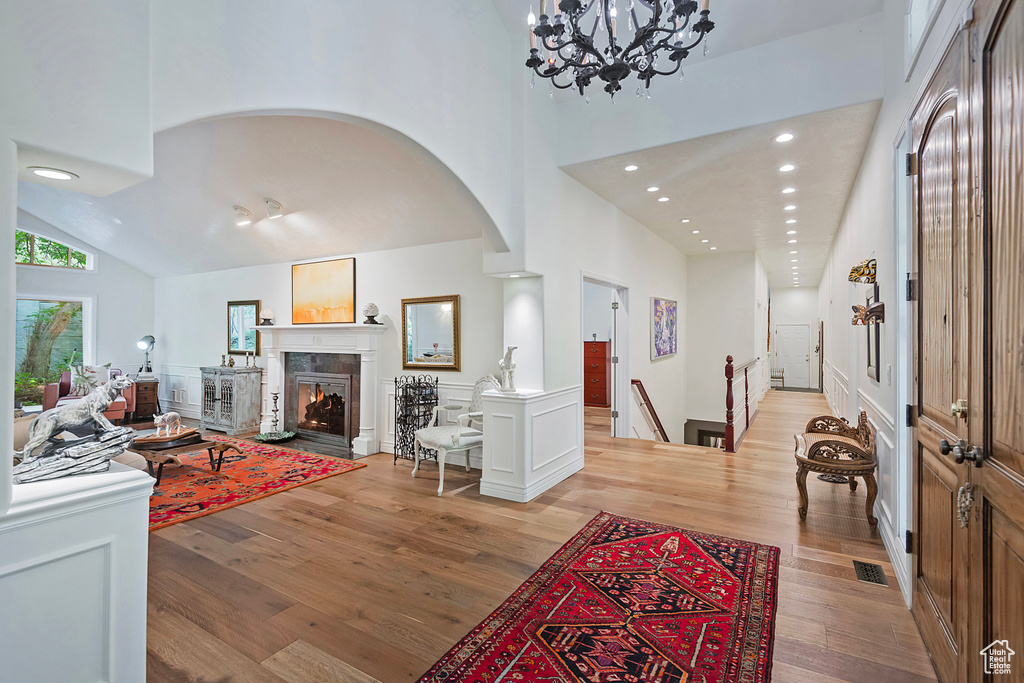 Living area with light wood-style floors, high vaulted ceiling, a warm lit fireplace, arched walkways, and recessed lighting