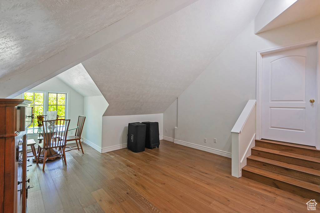 Additional living space featuring vaulted ceiling, hardwood / wood-style floors, baseboards, and a textured ceiling