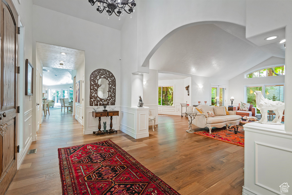 Living area with arched walkways, light wood-style flooring, high vaulted ceiling, wainscoting, and a chandelier