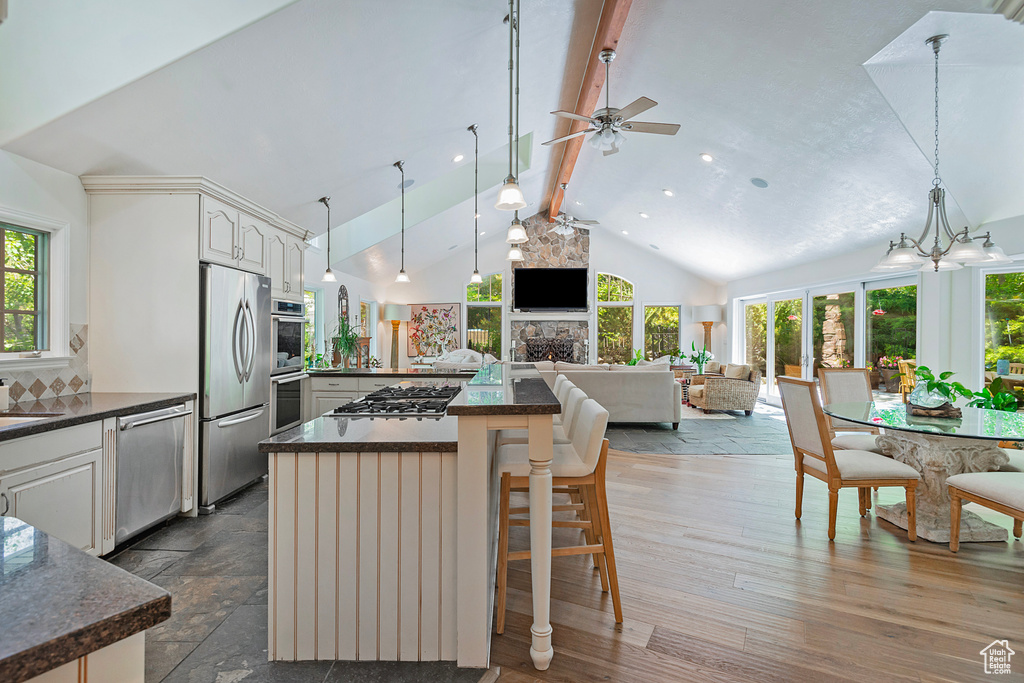 Kitchen featuring appliances with stainless steel finishes, open floor plan, beam ceiling, a ceiling fan, and a center island