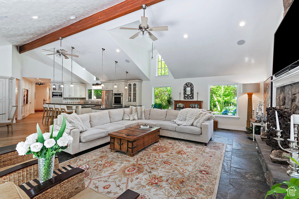 Living area featuring a ceiling fan, high vaulted ceiling, beam ceiling, healthy amount of natural light, and baseboards
