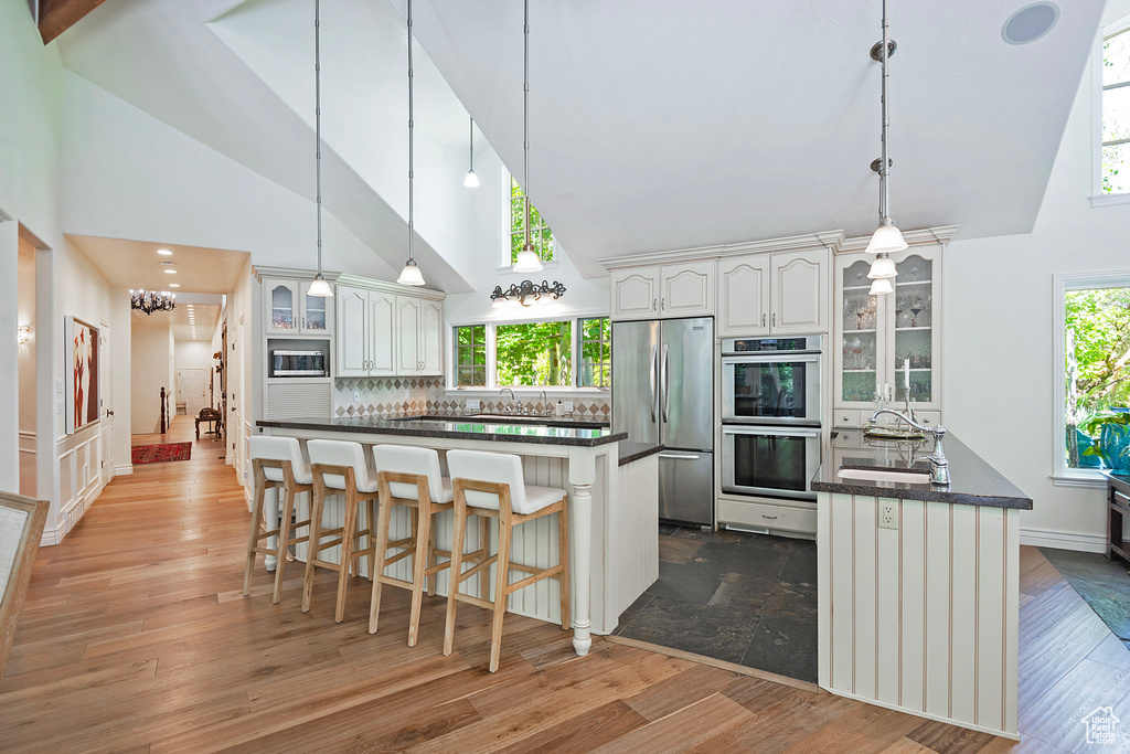 Kitchen with stainless steel appliances, high vaulted ceiling, glass insert cabinets, a kitchen bar, and decorative backsplash