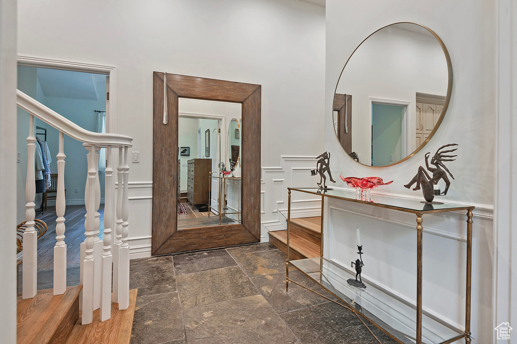 Entrance foyer featuring a decorative wall, stairway, a wainscoted wall, and stone tile floors