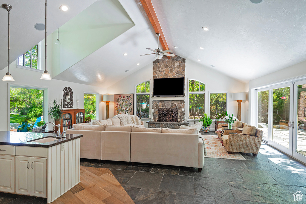 Living room featuring a fireplace, ceiling fan, stone tile flooring, plenty of natural light, and high vaulted ceiling