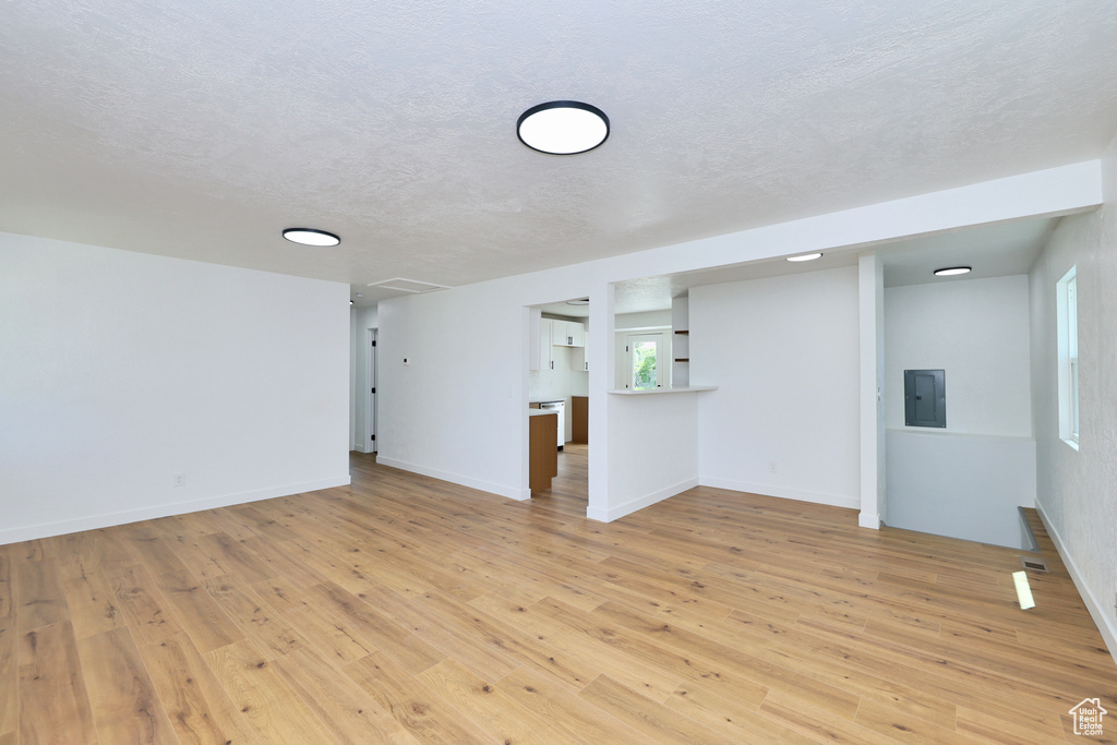 Spare room featuring electric panel, light wood finished floors, healthy amount of natural light, a textured ceiling, and baseboards