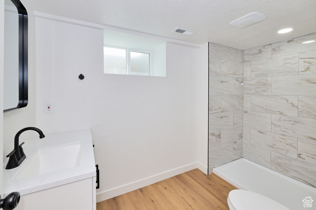 Bathroom with vanity, a tile shower, wood finished floors, toilet, and baseboards