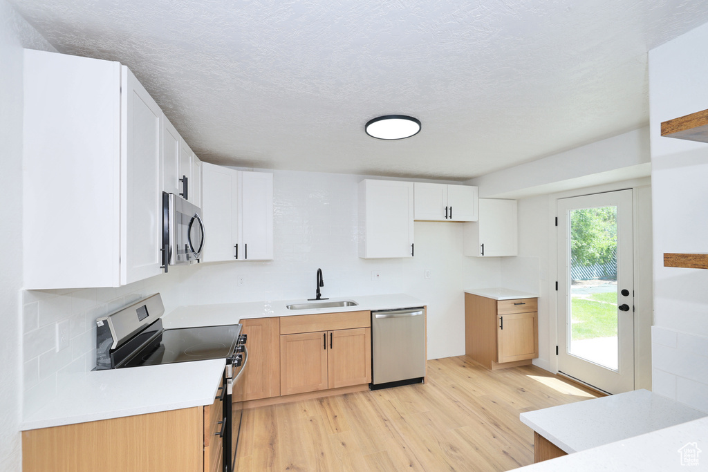Kitchen with stainless steel appliances, a sink, light wood-style floors, and white cabinetry