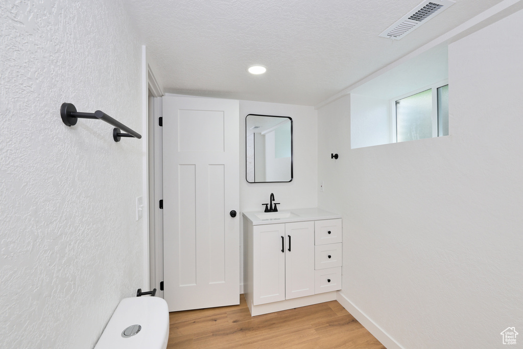 Bathroom with wood finished floors, vanity, toilet, a textured ceiling, and recessed lighting