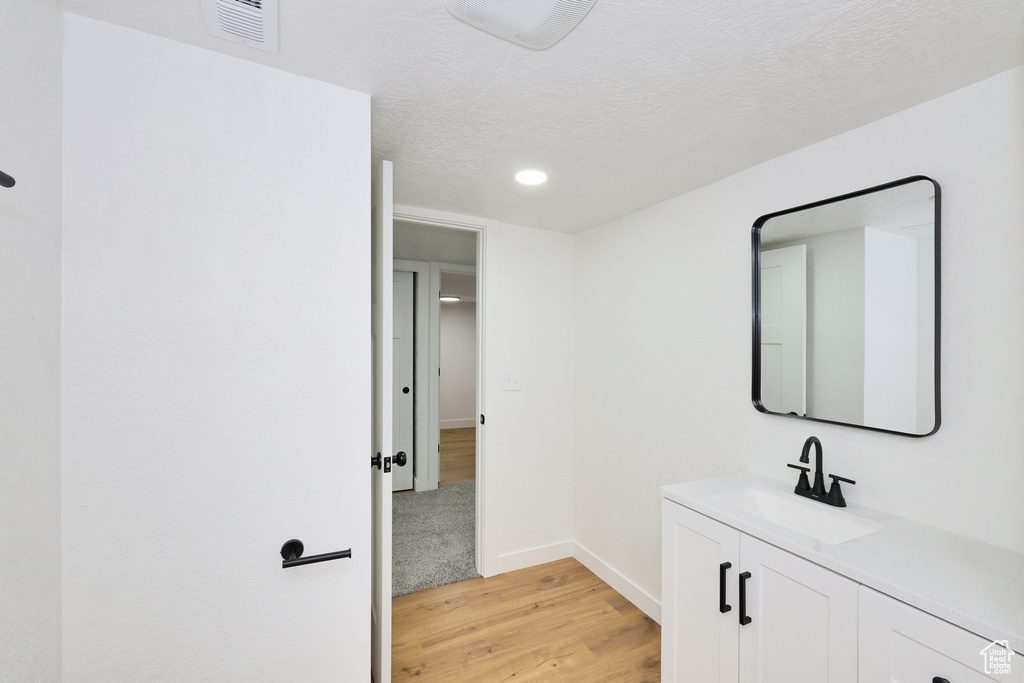 Corridor featuring a sink, light wood-type flooring, baseboards, a textured ceiling, and recessed lighting