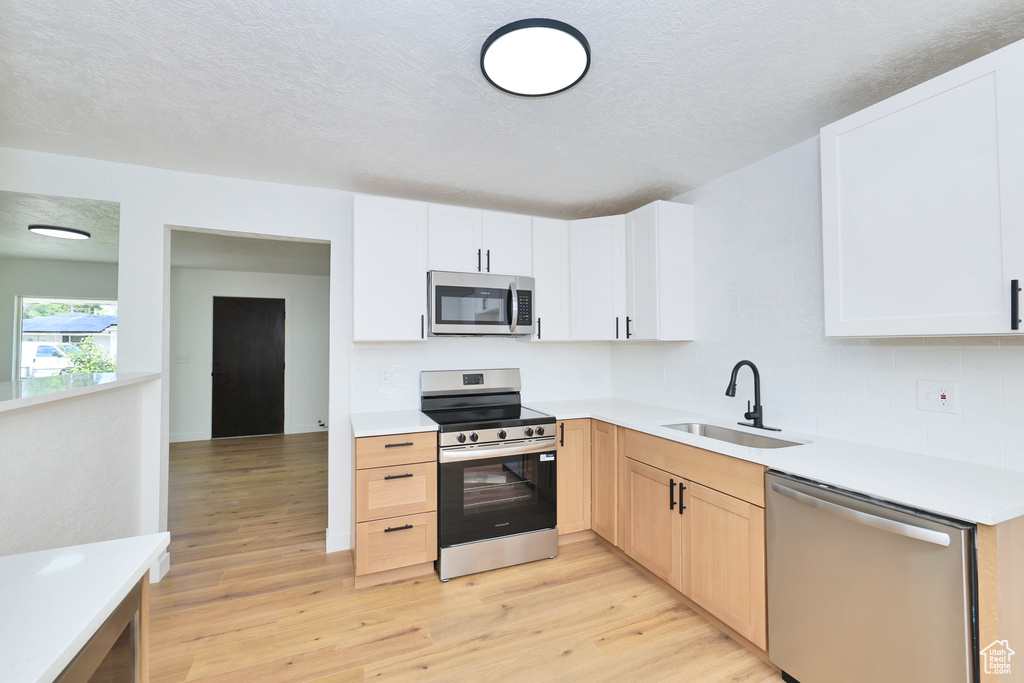 Kitchen featuring stainless steel appliances, a sink, light wood-style flooring, tasteful backsplash, and light countertops