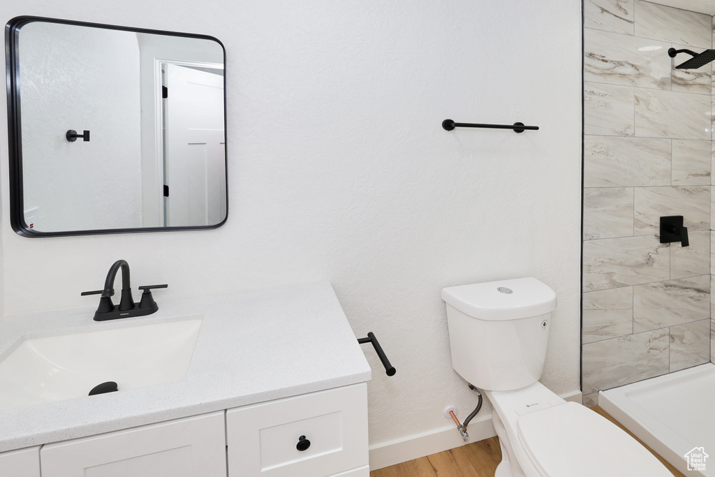 Bathroom with toilet, vanity, a tile shower, wood finished floors, and baseboards