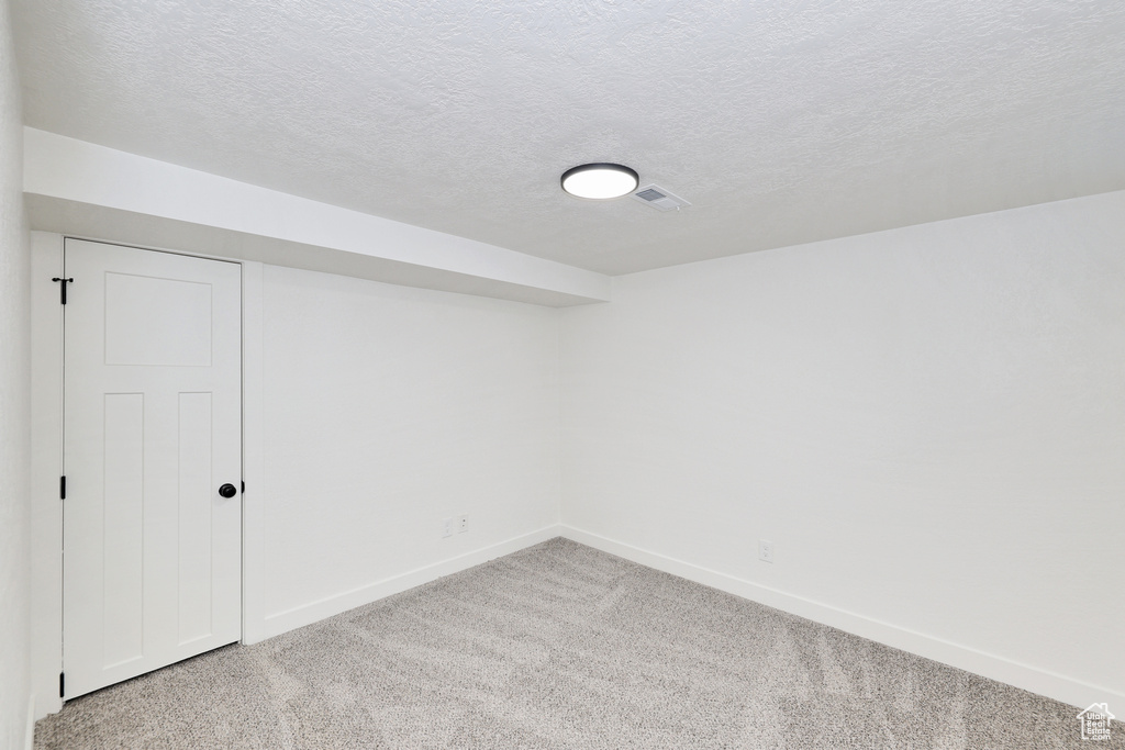 Spare room with light carpet, baseboards, and a textured ceiling