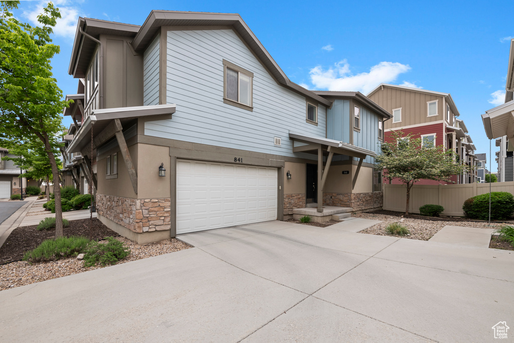 Multi unit property featuring stone siding, driveway, fence, and a garage