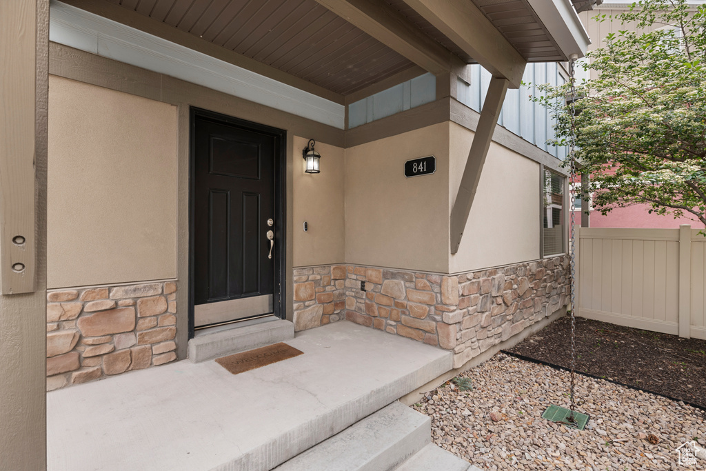 View of exterior entry with stone siding, stucco siding, and fence