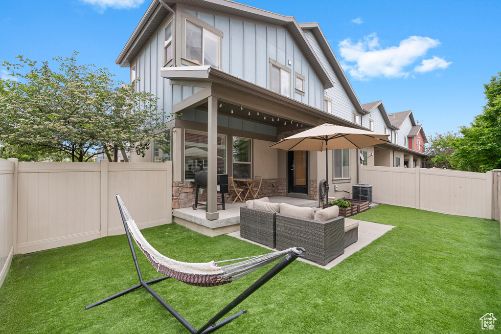 Back of property with board and batten siding, an outdoor hangout area, a patio, stone siding, and central air condition unit