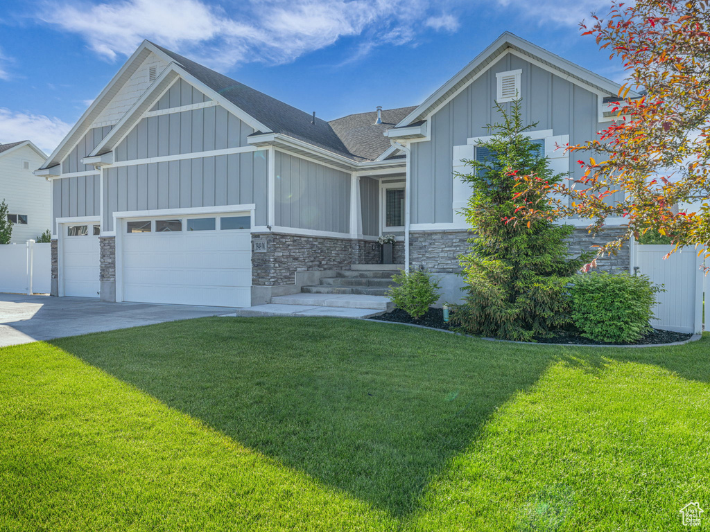 View of front facade with board and batten siding, stone siding, roof with shingles, an attached garage, and concrete driveway