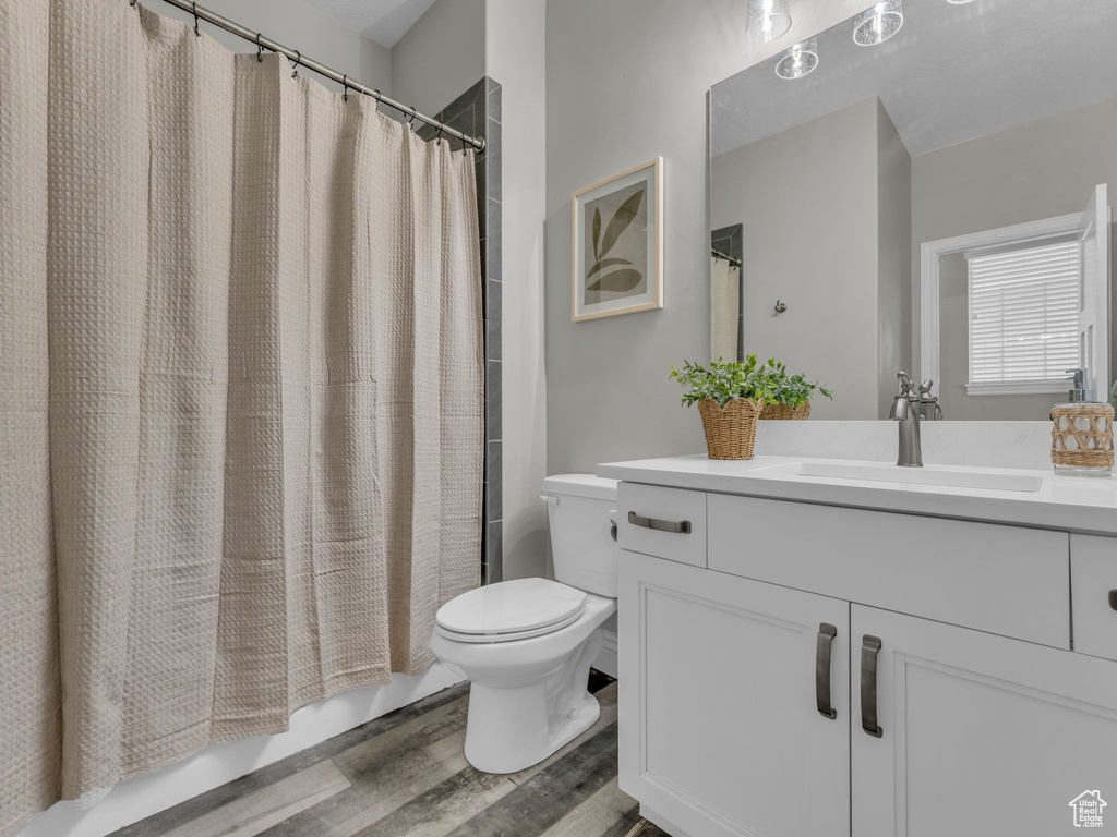 Full bath featuring toilet, vanity, wood finished floors, and shower / bath combination with curtain
