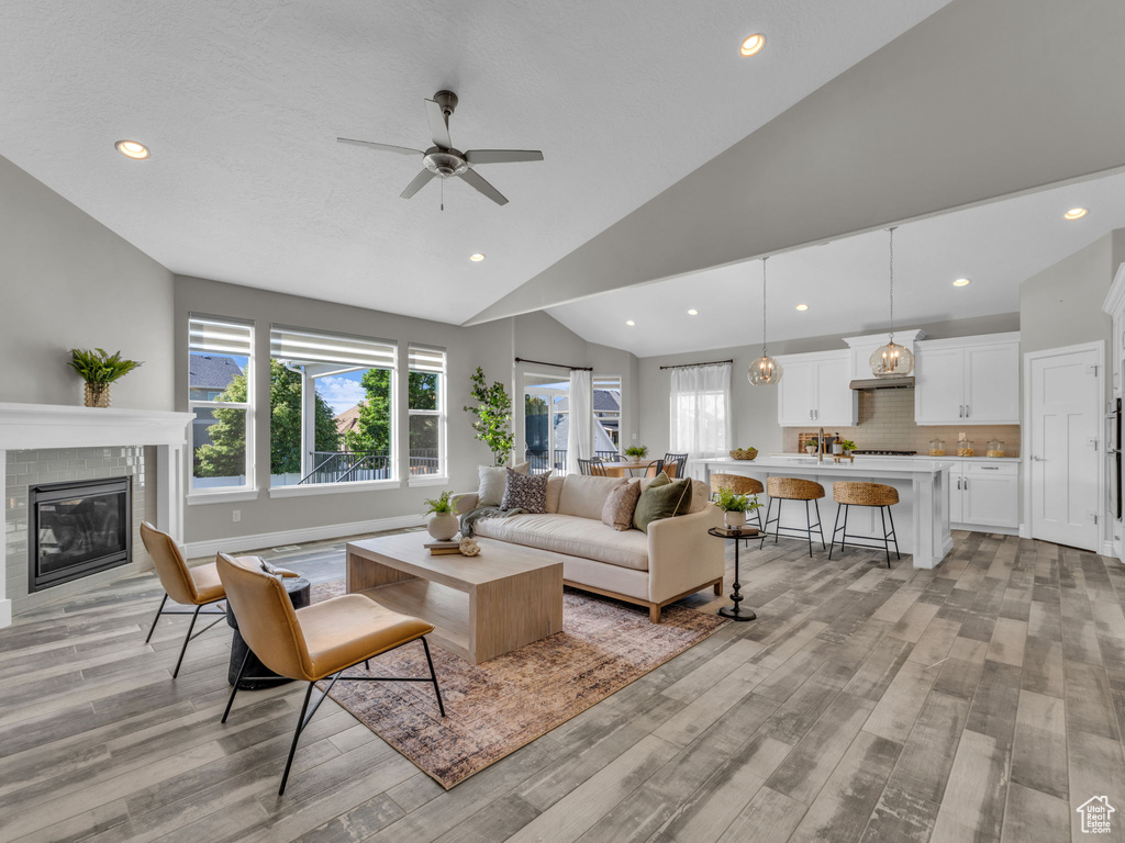 Living area with light wood-style flooring, lofted ceiling, a tile fireplace, a ceiling fan, and recessed lighting
