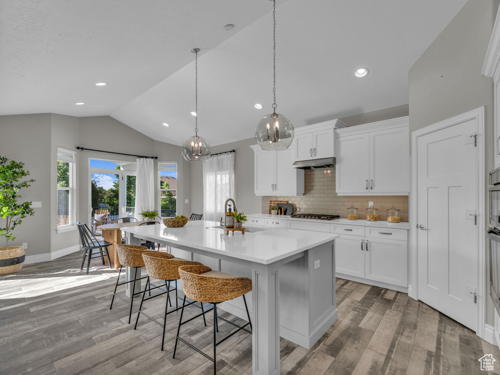 Kitchen with lofted ceiling, light wood-style floors, under cabinet range hood, light countertops, and backsplash