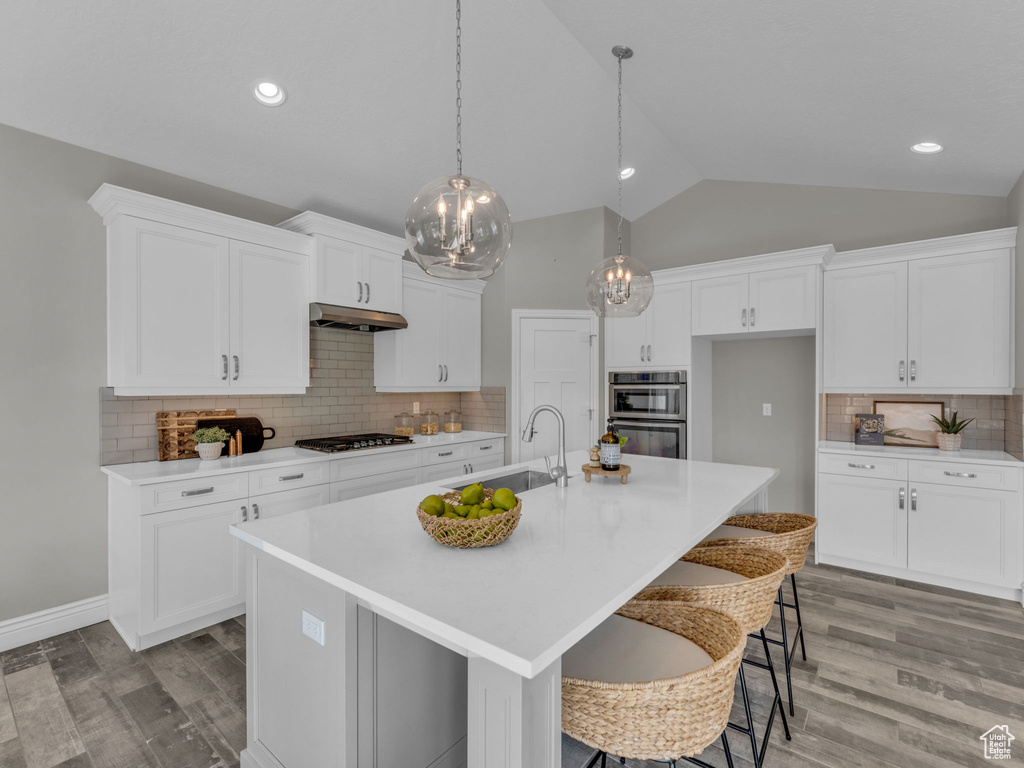 Kitchen with a sink, under cabinet range hood, gas stovetop, light countertops, and white cabinetry