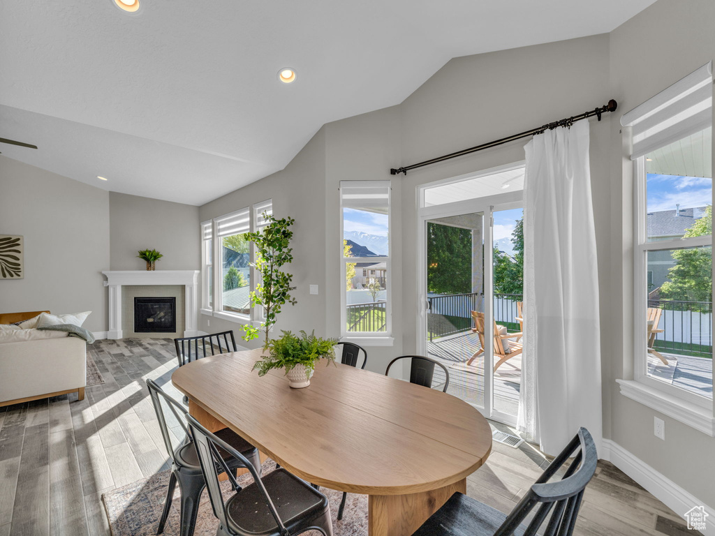 Dining room with lofted ceiling, light wood-style flooring, a glass covered fireplace, baseboards, and recessed lighting